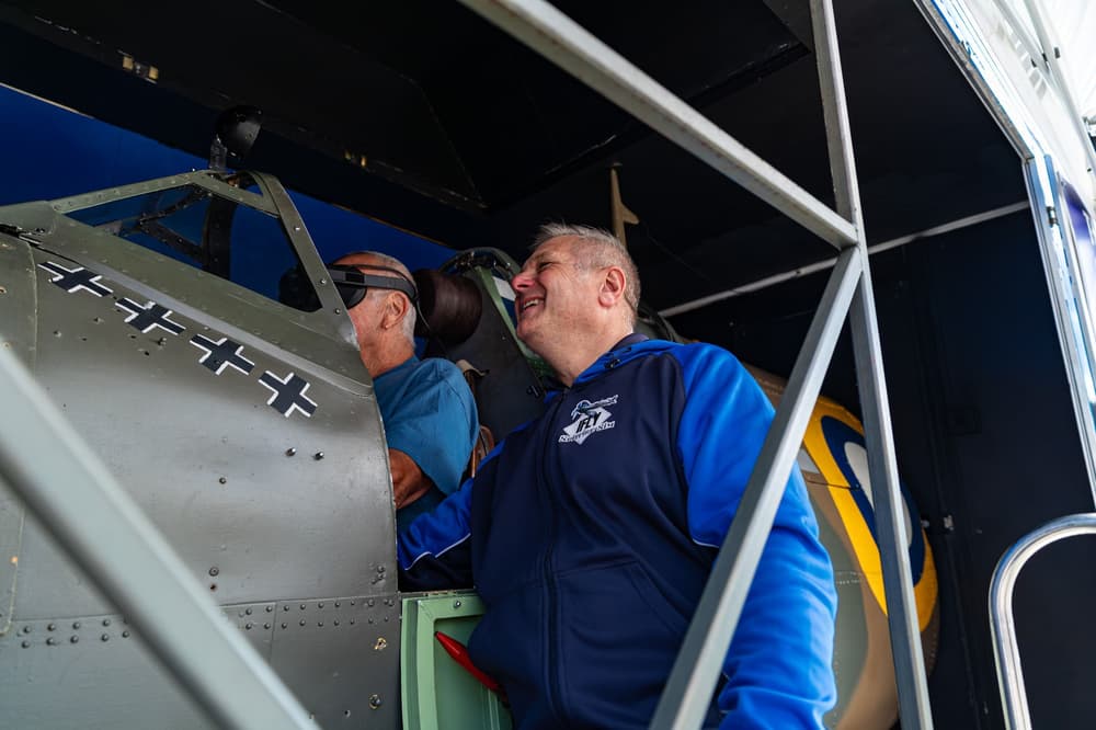 man in a spitfire flight simulator with another man looking on