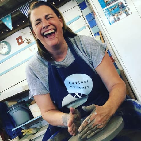woman laughing while moulding clay on a potters wheel on a pottery experience day