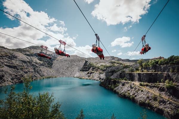 people on the zip lines at zip world velocity in wales going over the quarry lake