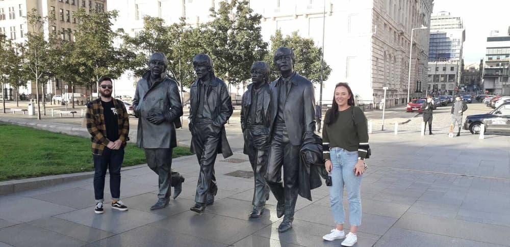 people posing for a photo next to the statues of the beatles seen on the 60 minute beatles tour in liverpool