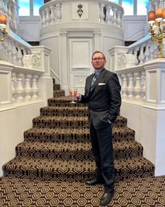 man wearing smart suit holding a martini in front of a grand staircase as part of james bond tour