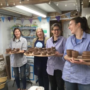 four ladies in a pottery workshop holding boards with their clay creations made during a pottery course experience day.