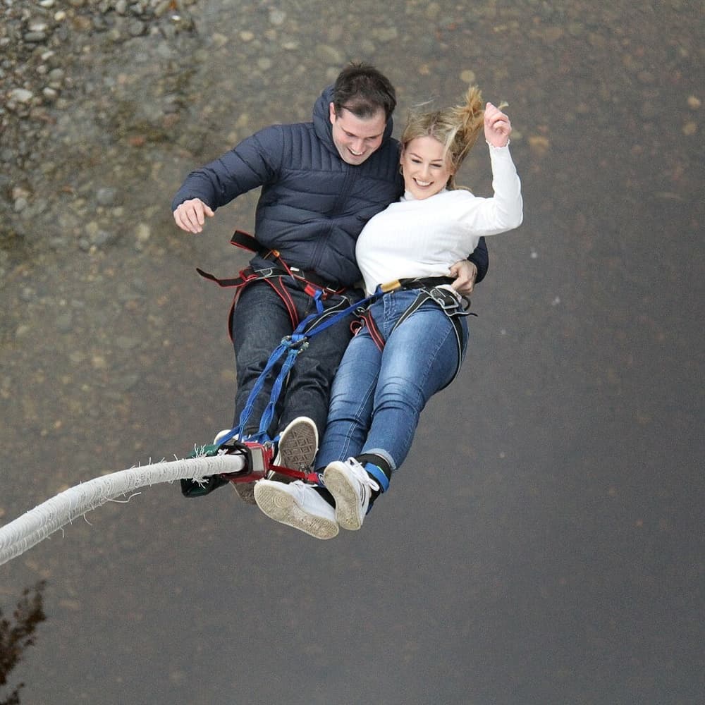 couple doing a tandem bungee jump over a river on a bungee jump experience day