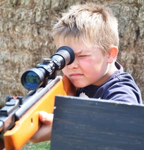 young boy aiming an air rifle on a spy camp experience day for kids
