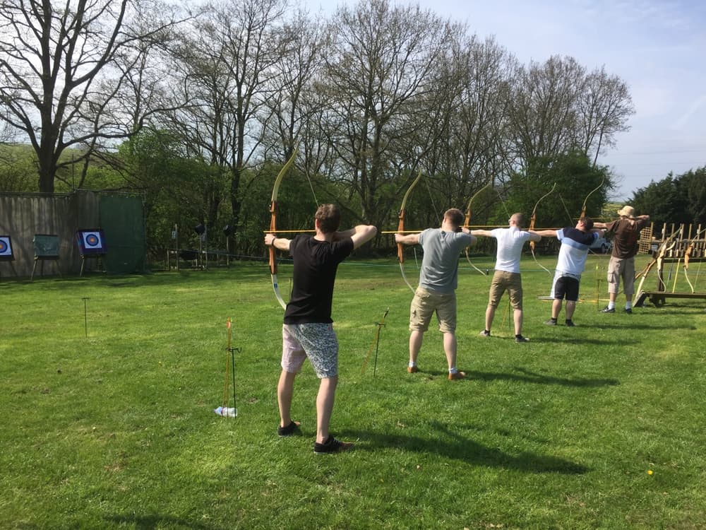 a row of people holding bows and arrows aiming at targets as part of an archery experience