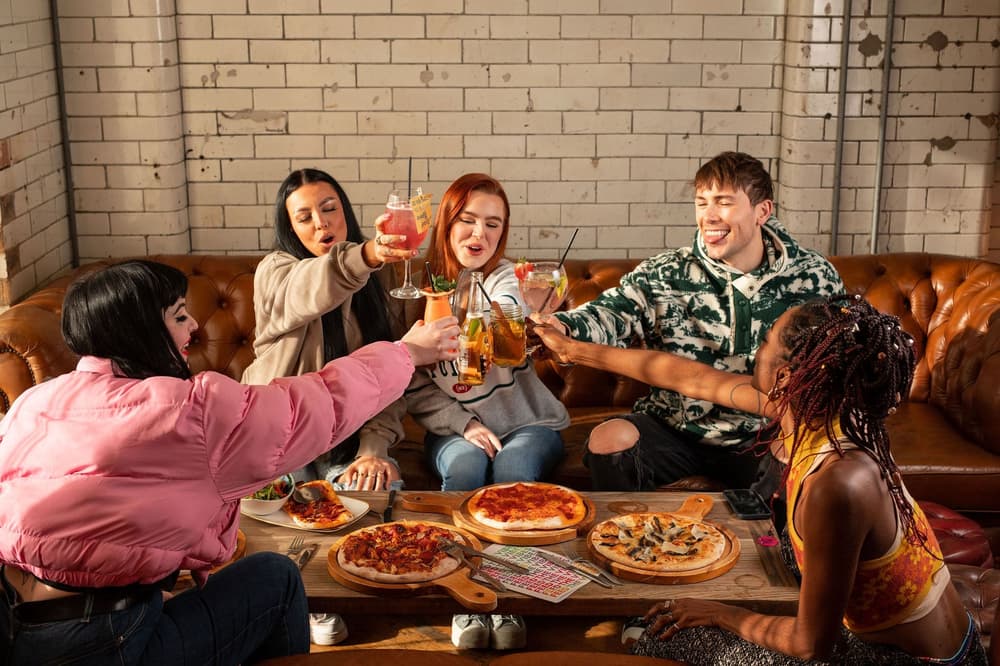 a group of 5 clinking drinks with pizza