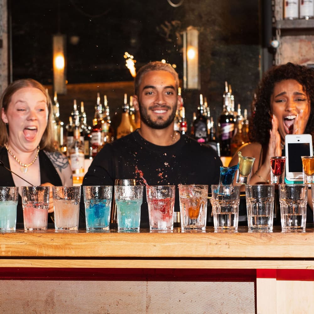3 bartenders looking at a line of cocktails with excitement