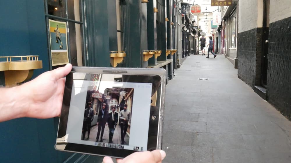 hands holding a photo of the beatles in the same alleyway where the photo was taken seen on the beatles walking tour