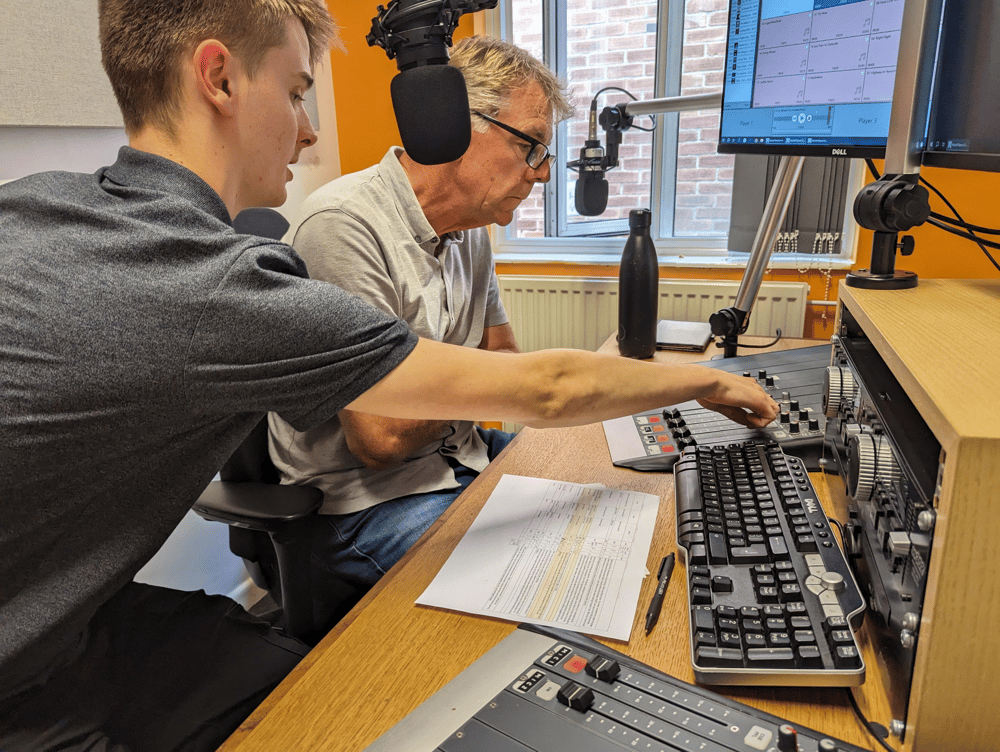 two men sat in front of a microphone at a radio station on a record your own show experience