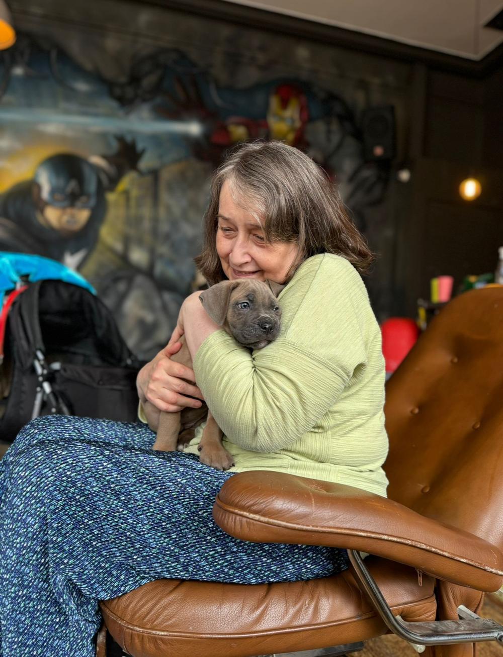 a woman sitting on an armchair holding a puppy on a puppy therapy experience
