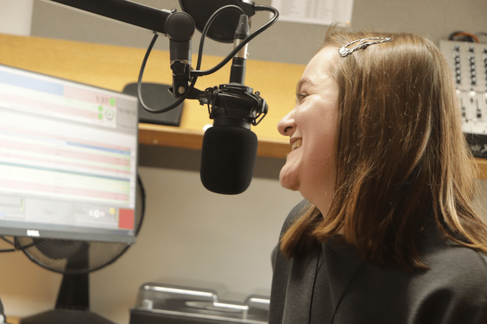 woman sat in front of a microphone at a radio station on a record your own show experience