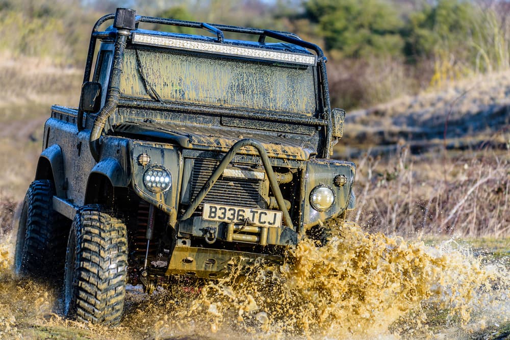 a mad max inspired land rover driving off road through a muddy puddle on a driving experience day