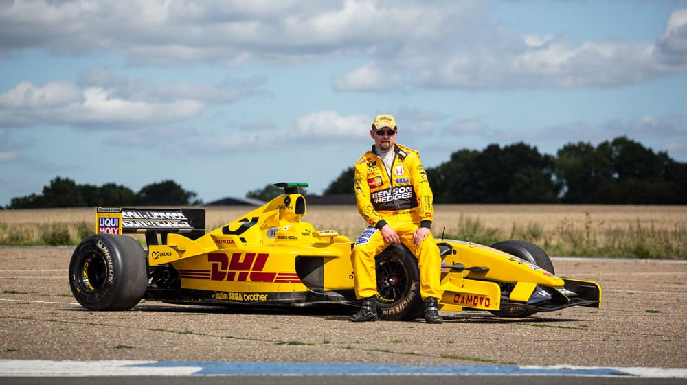 man in yellow driving suit sat on an f1 jordan car on a f1 car photoshoot and passenger lap experience