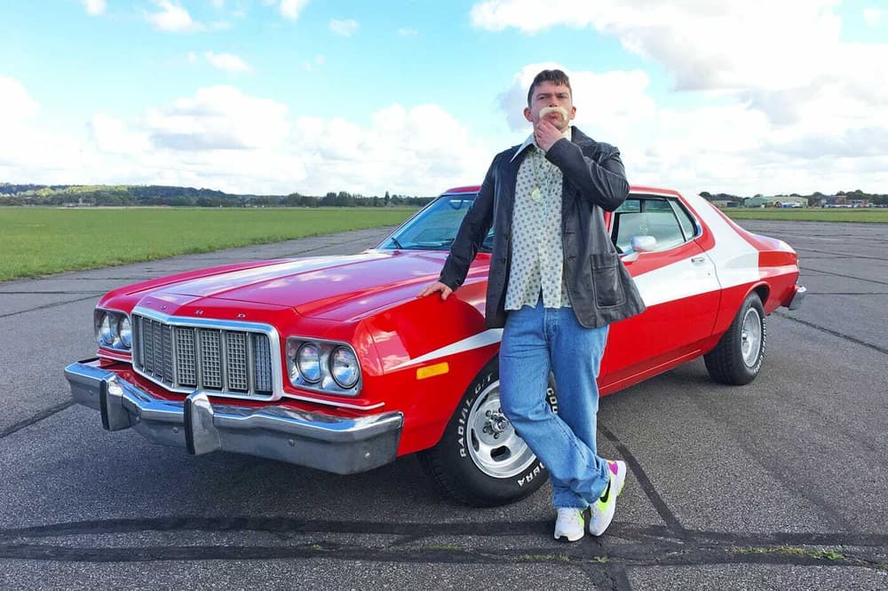 a man standing next to a red vintage car on a track as part of a movie cars driving experience day
