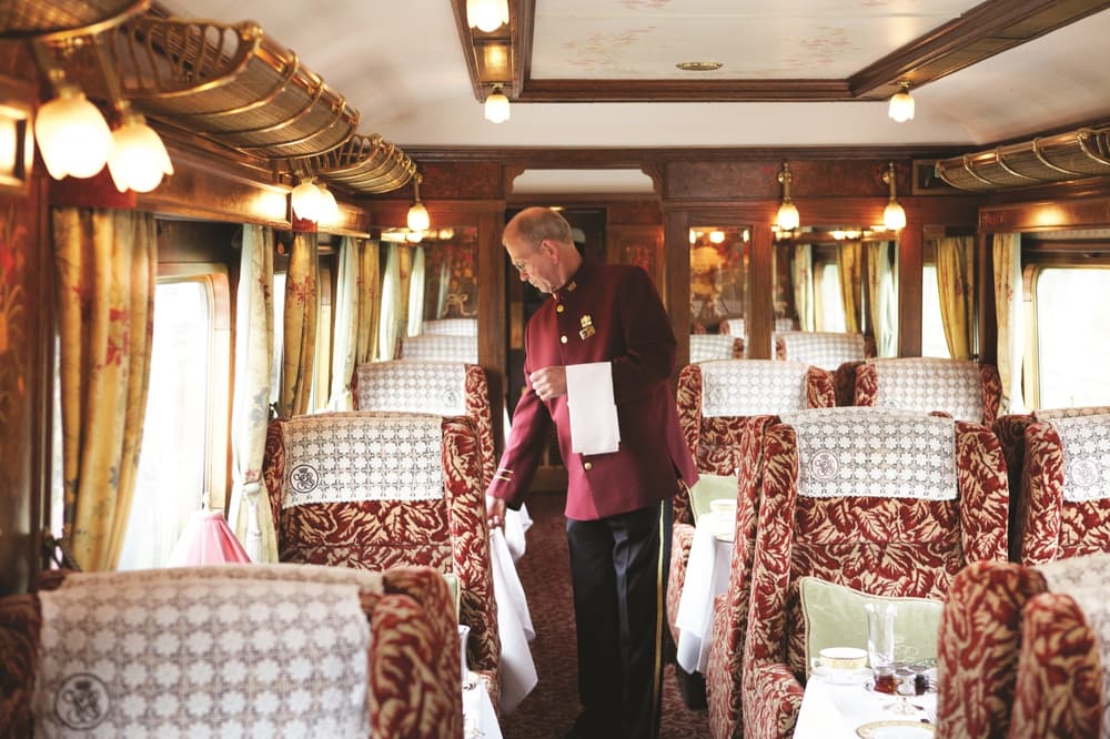 a train steward in traditional smart uniform checking the tables on a vintage style northern belle train carriage