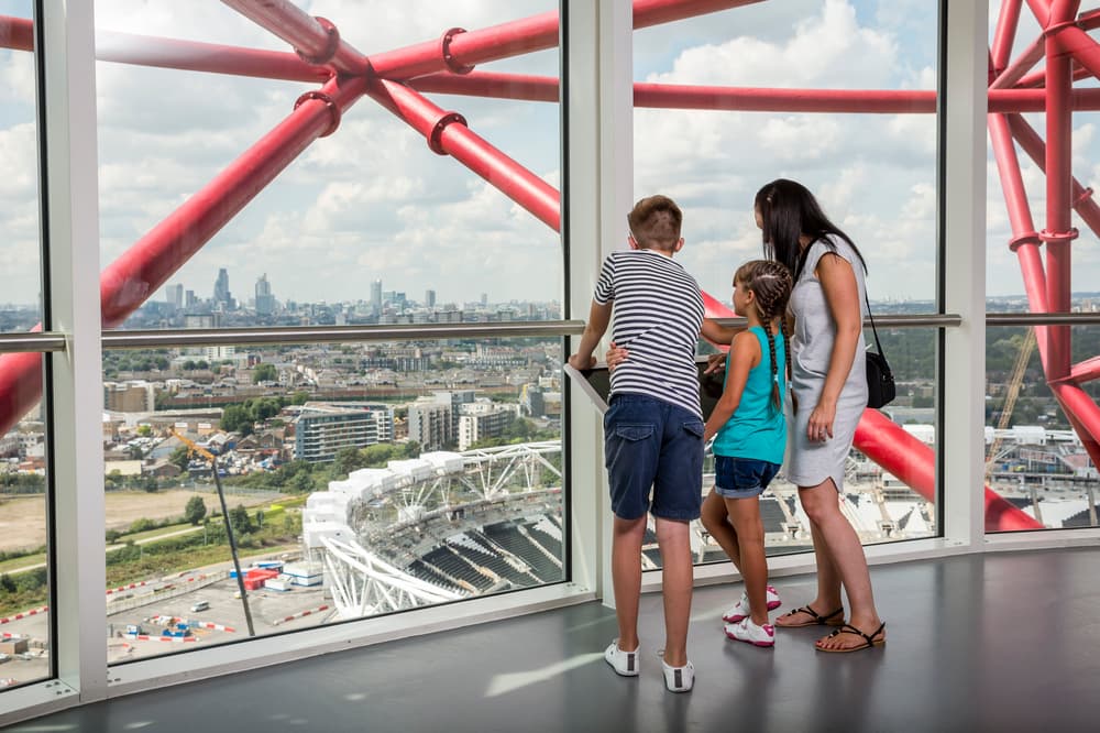 a woman and two children looking out over london at the top of the arcelormittal orbit