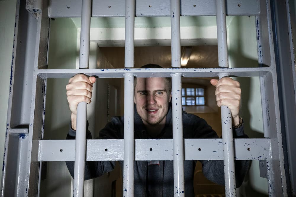 a man looking through and holding onto a prison cell door on a prison escape room experience day