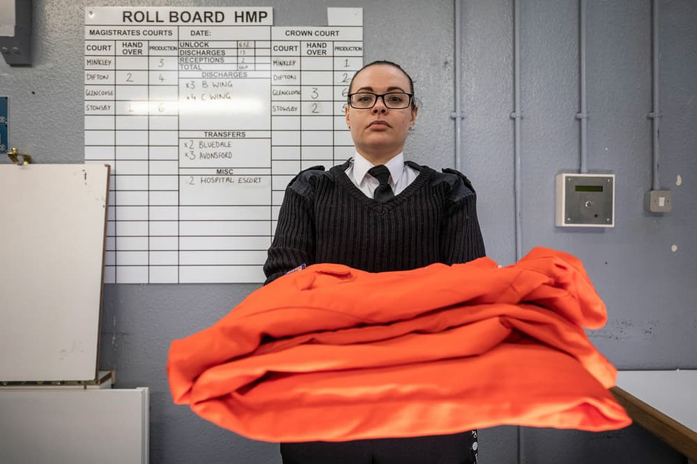 a guard handing over orange overalls as part of a prison break experience day