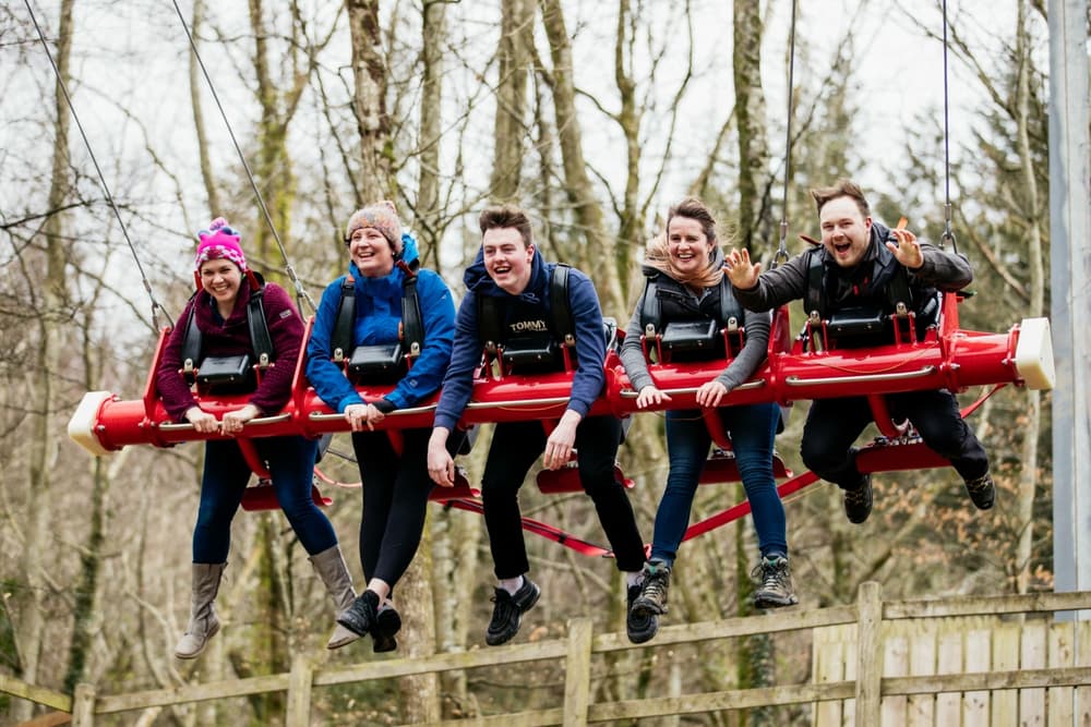 people on a giant swing above the tree tops as part of a skyride experience at zip world