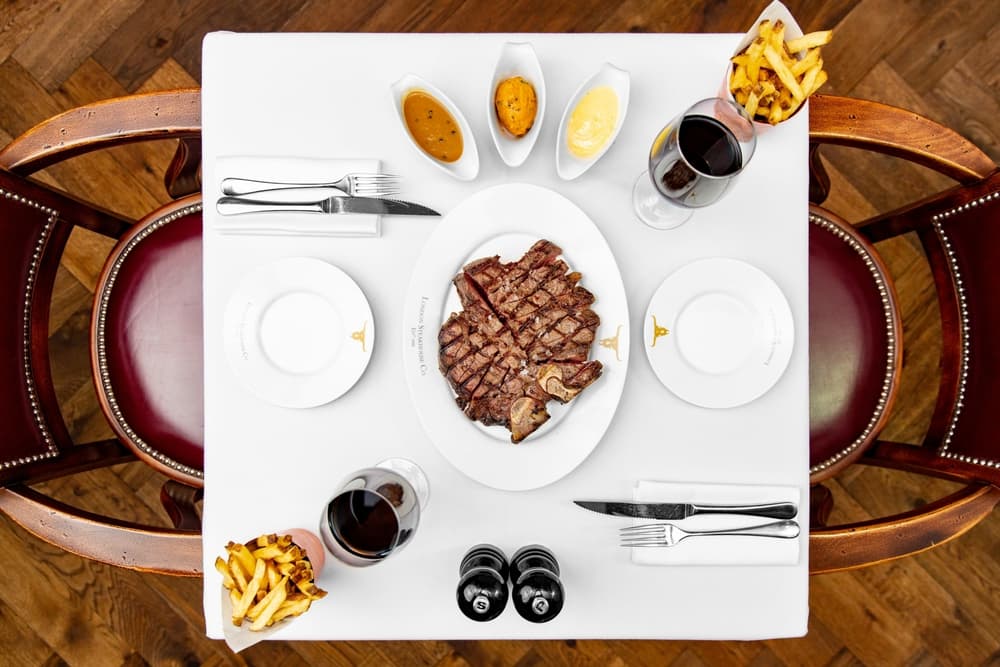 a view from above of a restaurant table laid out with a plate of steak in the middle, fries and sauces on the side