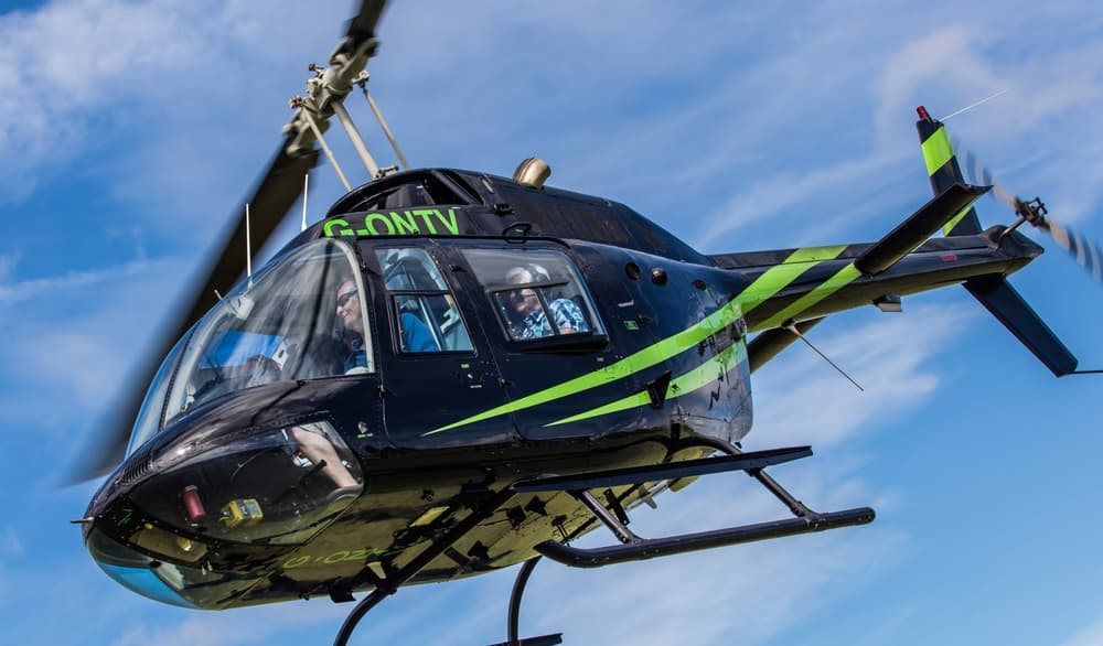 a black helicopter with green stripes in the air for a helicopter ride experience with adventure 001
