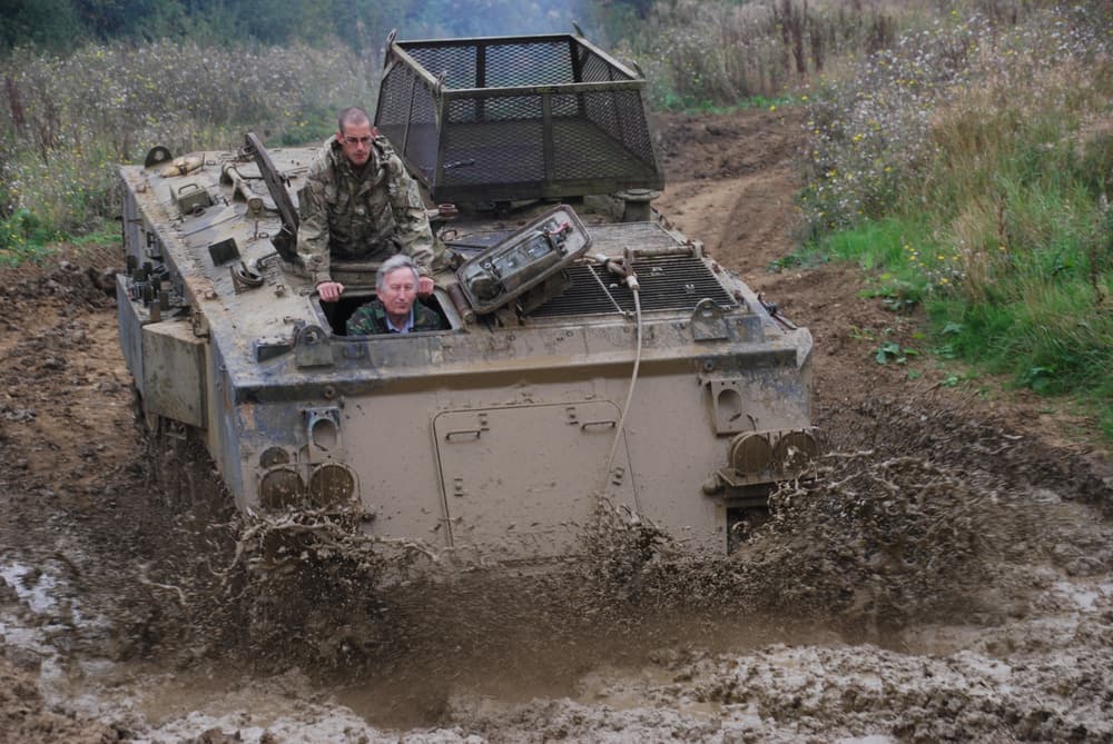 a military tank being driven through a muddy puddle on a tank driving experience day