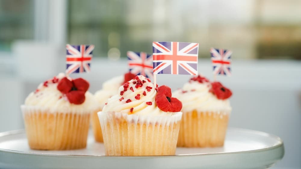 4 cupcakes topped with white icing and strawberries and union jack flags for the king's coronation