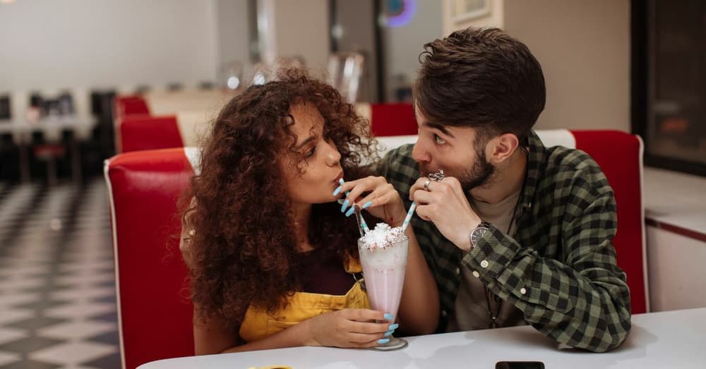 man and woman sharing a milkshake on a date night in an american style diner