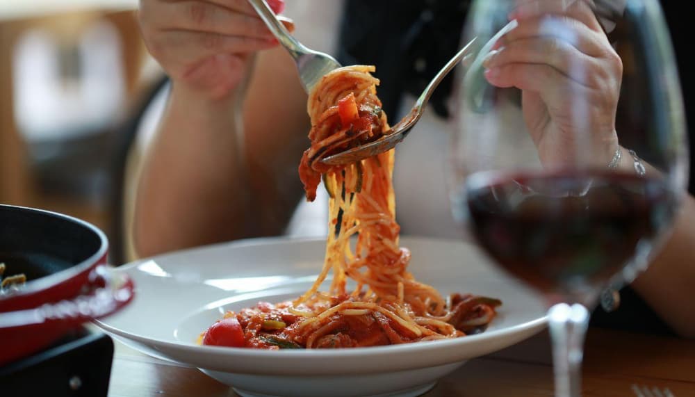 a woman eating pasta on the outside terrace of a restaurant in italy on a sunny day