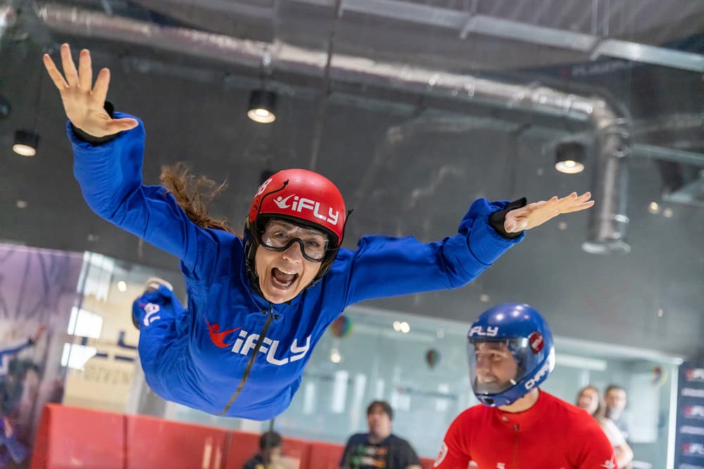 a woman wearing a blue flight suit, goggles and helmet on an indoor skydiving experience