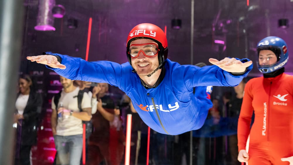 a man wearing a blue flight suit, goggles and helmet on an indoor skydiving experience