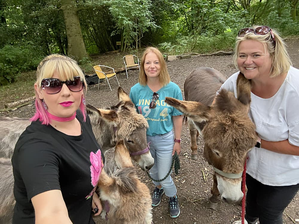 three women standing with donkeys in the woods on a donkey walk experience
