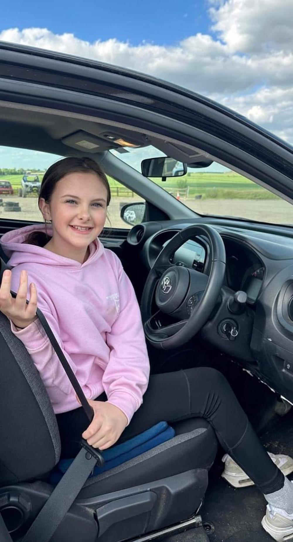 a young girl in the drivers seat of a car on a junior driving experience