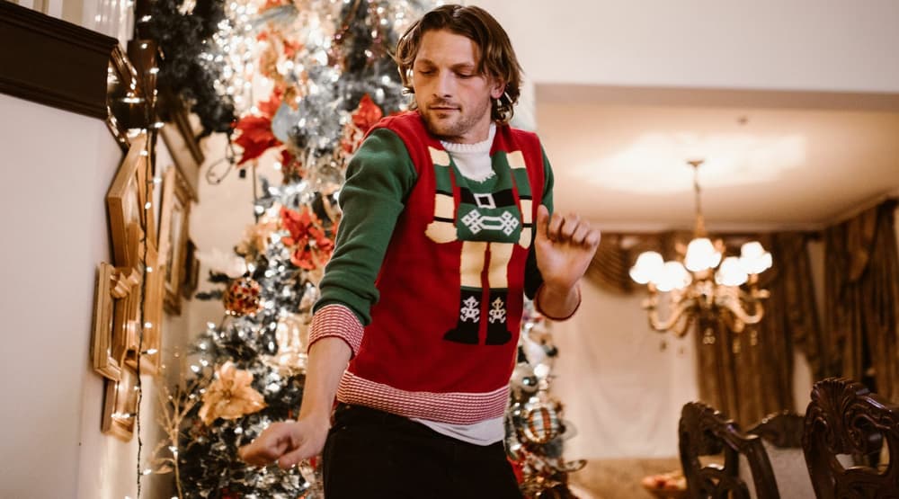 Man dancing wearing a christmas jumper infront of a christmas tree