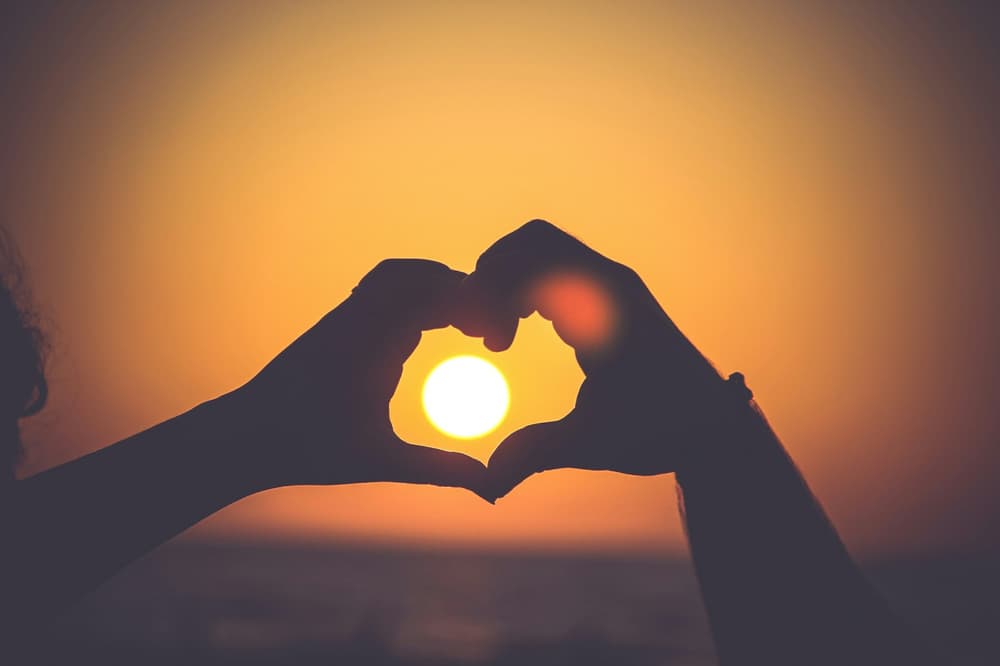two hands making a heart shape with the setting sun in the background