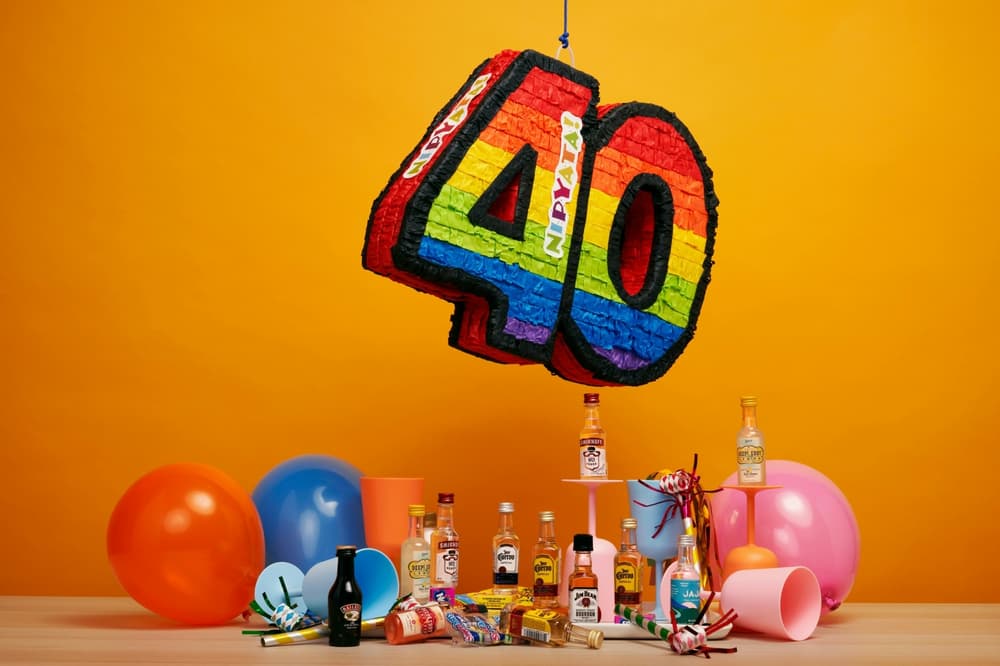 a colourful pinata shaped in the number forty hanging over a selection of party drinks and balloons