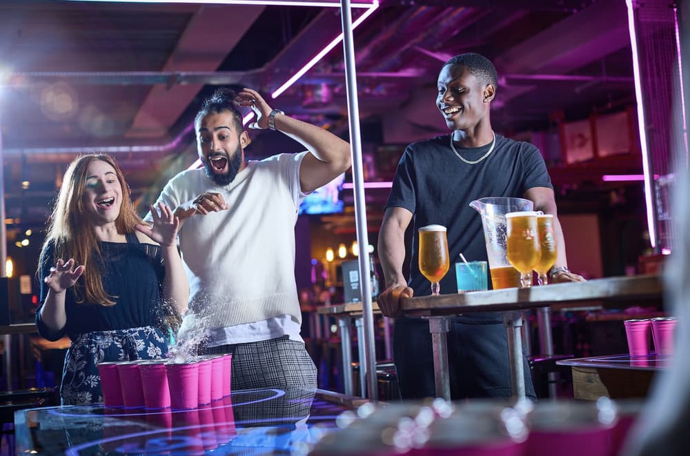 three people playing beer pong in a bar