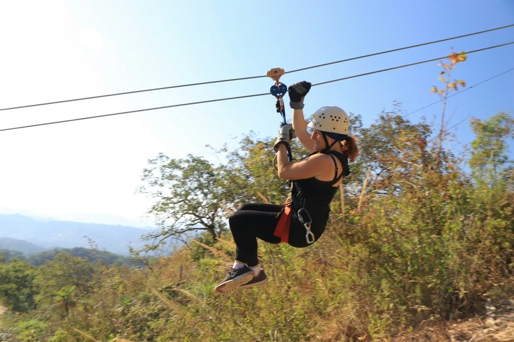 women on a zip line against trees and a sunny sky