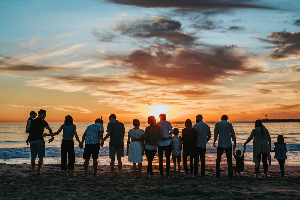 adults and children in a row holding hands on a beach at sunset