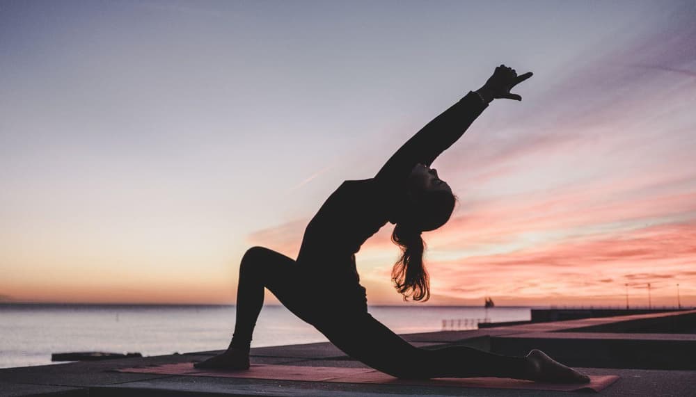 a woman kneeling on a yoga mat looking out at a sunset on a wellness experience