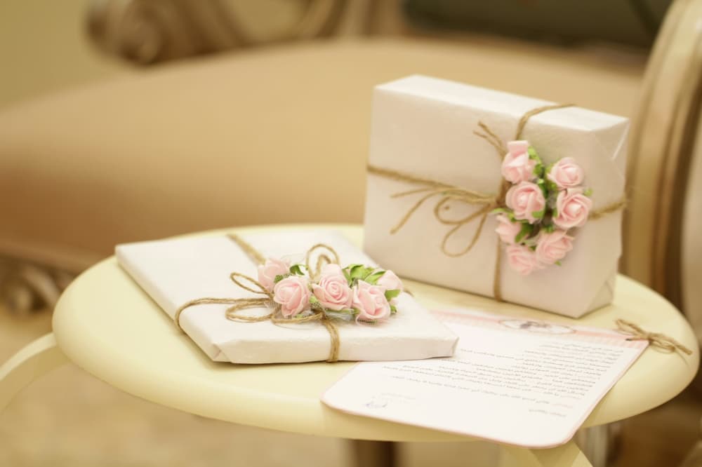 two presents wrapped in white paper with pink flowers attached on a small round table