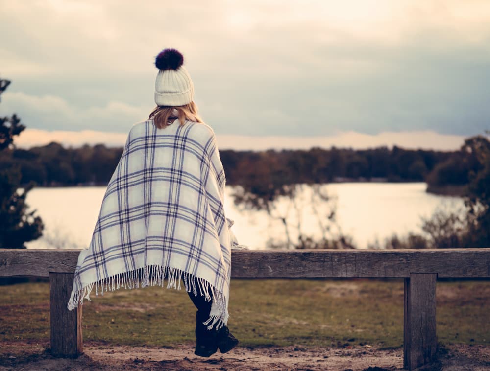 Woman wrapped in a blanket looking out of a cabin window