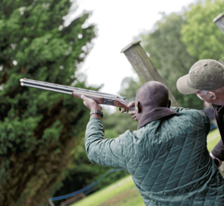 man pointing shotgun to the sky with instructor looking on as part of clay pigeon shooting experience