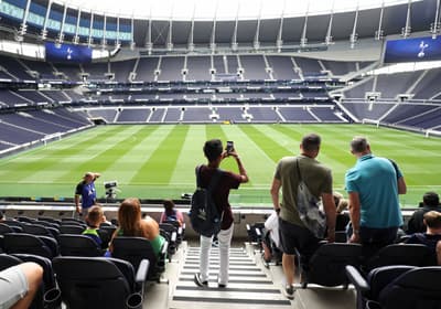visitors in the stands overlooking the pitch on the tottenham hotspur stadium tour in london