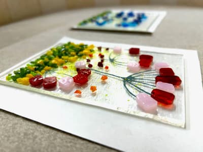 the front of a glass tea light holder with a coloured floral design laid on a board ready to go into the kiln