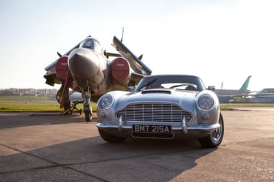 a british classic car next to an airplane on an airfield track