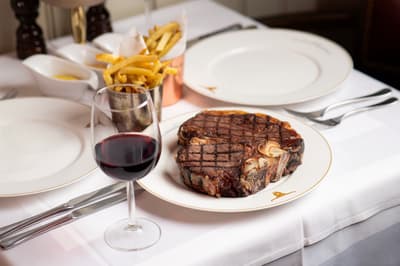 a steak meal with fries on the side and a glass of wine at marco pierre white's london steakhouse company