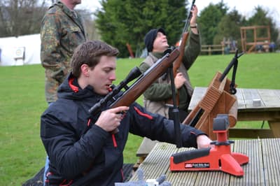 man sitting at table outside holding an air rifle as part of an air rifle shooting experience with instructor in background