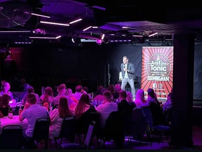 a comedian on stage with people looking on at a comedy night