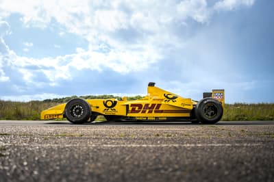 a side view of a yellow jordan formula one race car on a race track  against a cloudy sky background